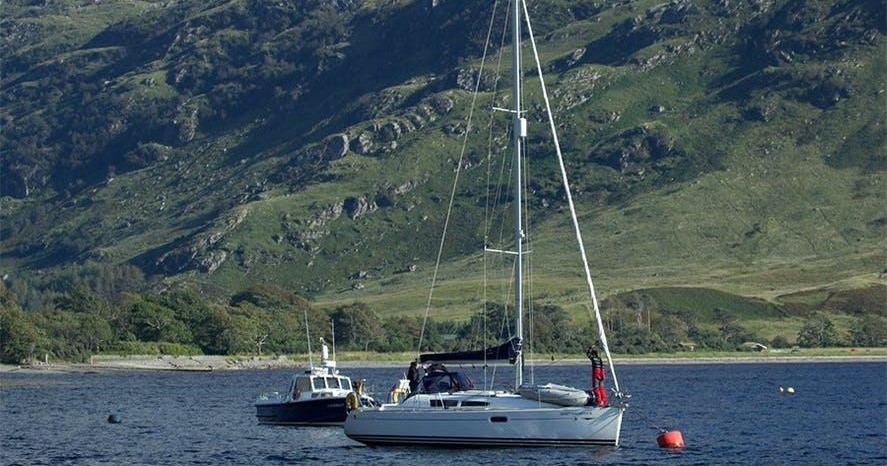 Sailboat and motorboat on a lake with hills in the background.