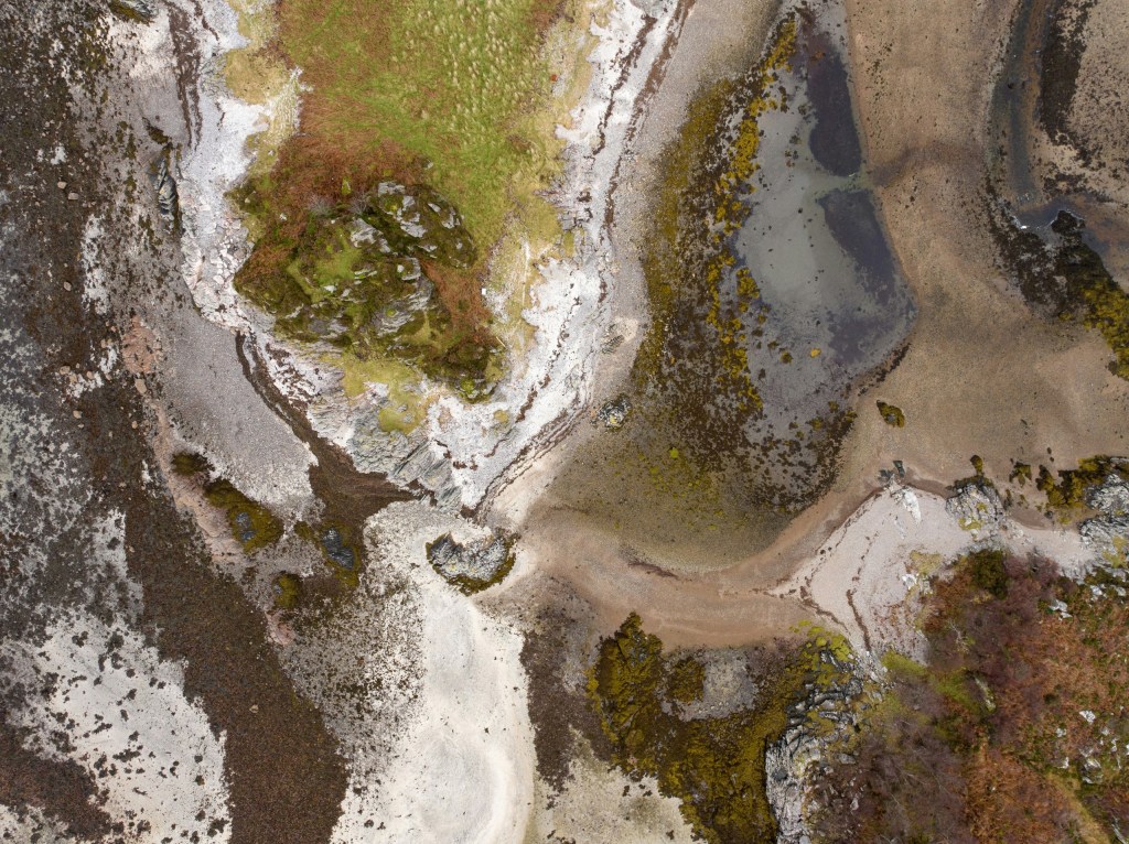 Aerial view of rocky coastline with green patches and sandy areas.