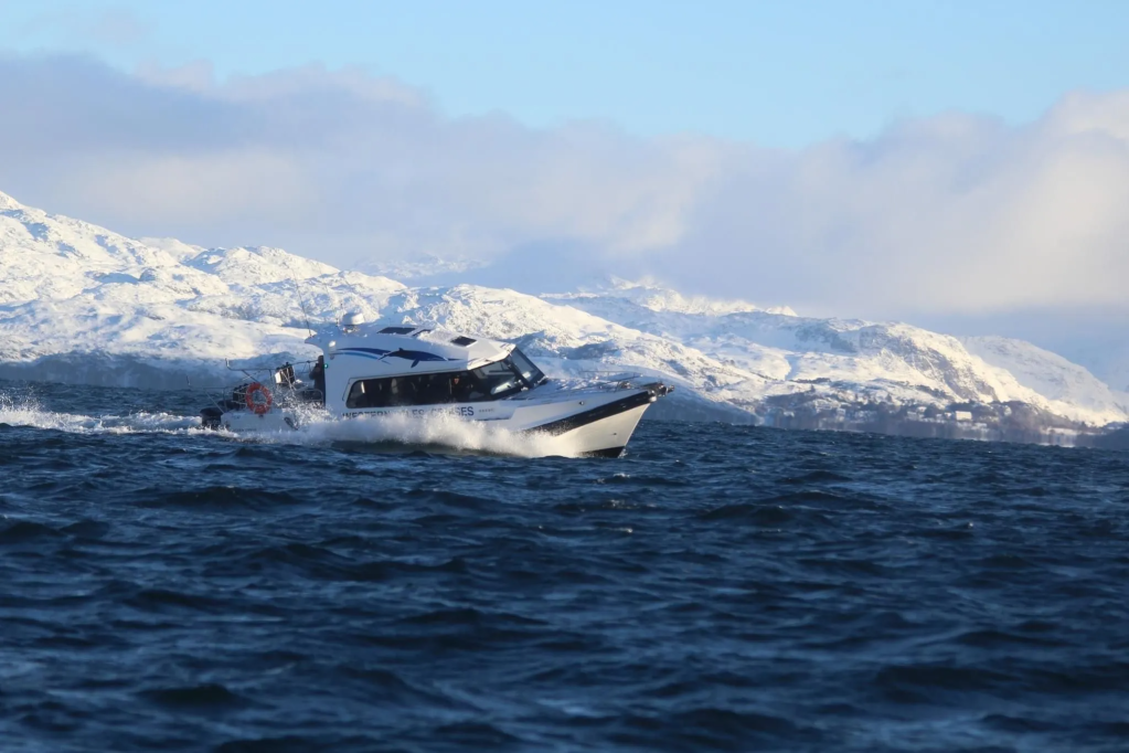 Boat on a large body of water with snow-covered mountains in the background.