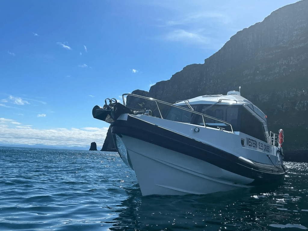 White boat on blue water near rocky cliffs under a clear sky.
