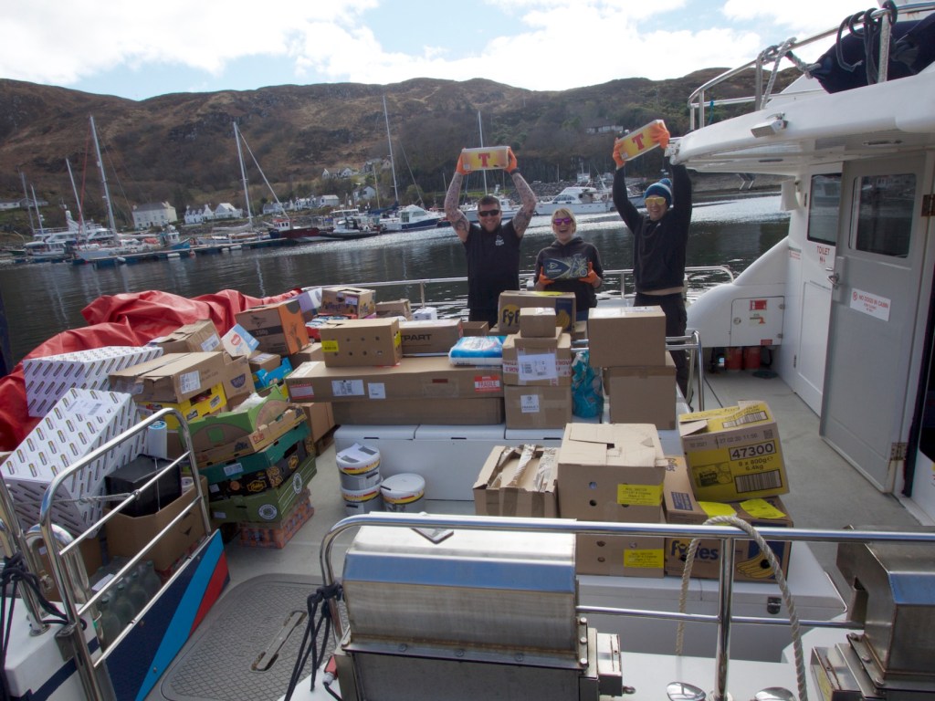 People on a boat with boxes and supplies in a marina.