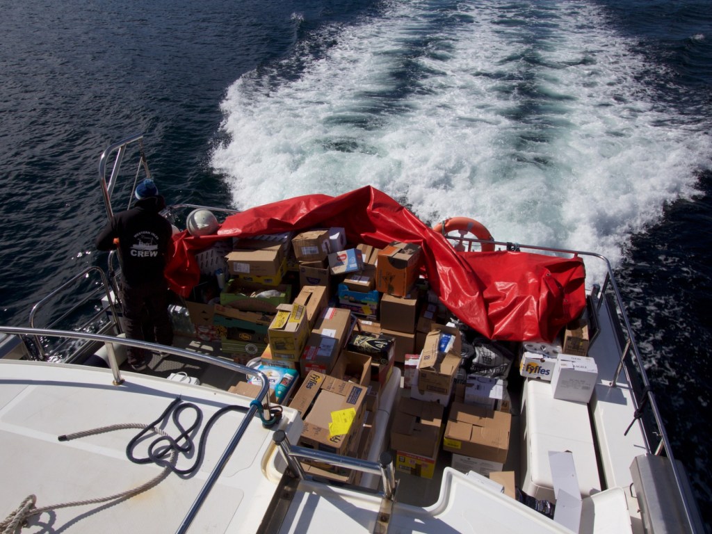 Boat carrying numerous boxes covered with a red tarp on ocean water.