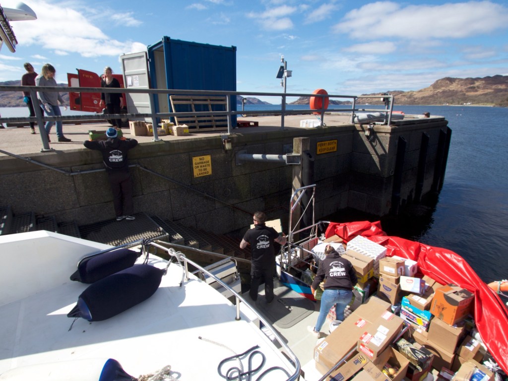 People loading boxes onto a boat from a dock on a sunny day.