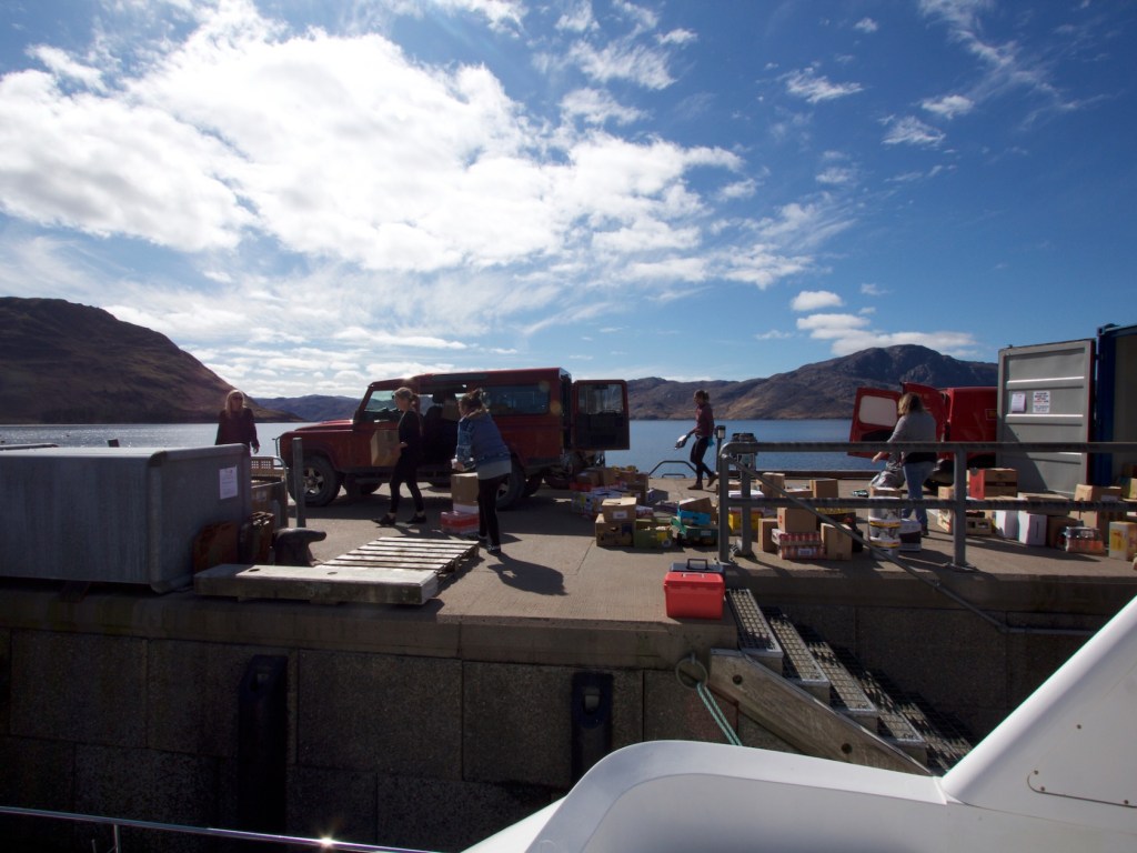 People unloading items from a red truck on a dock by a lake.