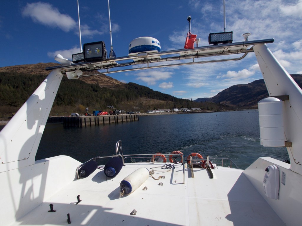 View from a boat's deck overlooking a calm lake and distant hills.