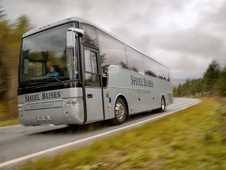 imgi_9_bus Grey tour bus driving on a winding road with blurred trees.