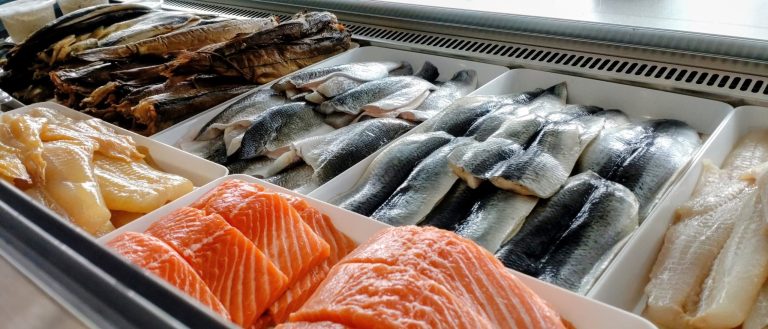 Variety of fresh fish fillets displayed on ice in a seafood market.