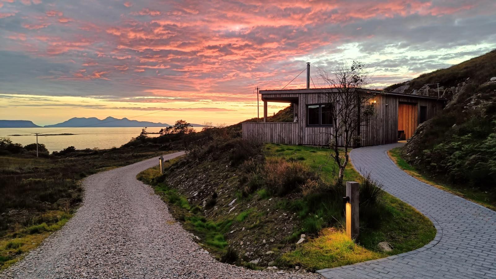 Cottage on hill at sunset with winding paths and sea view.