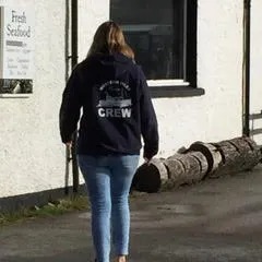 Person in crew jacket and jeans walking near seafood restaurant.