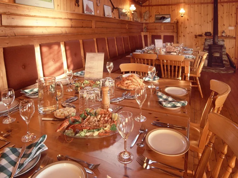 Long wooden dining table set with plates, glasses, and food in a rustic room.