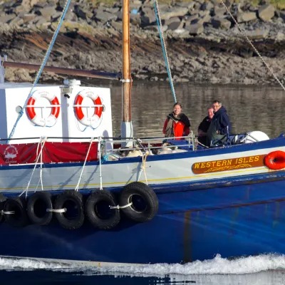 Blue boat named 'Western Isles' with three people on board, near rocky shore.