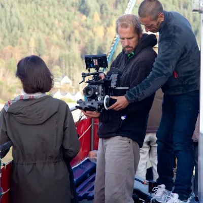Cameraman filming a person with forest in the background.