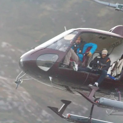 Helicopter flying with open door, two people visible inside.