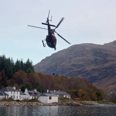 Helicopter flying over houses near a lake and mountains.