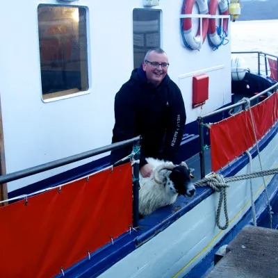 Person on ferry with a sheep, near red barriers, holding an animal.