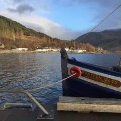 Boat docked by a lake with hills and houses in the background.