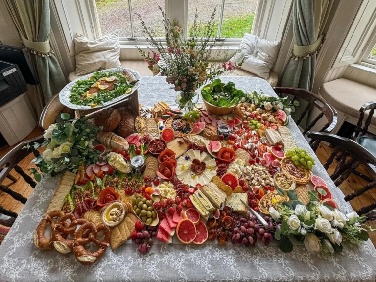 A large, colorful charcuterie spread on a table with meats, cheeses, fruits, vegetables, and breads.