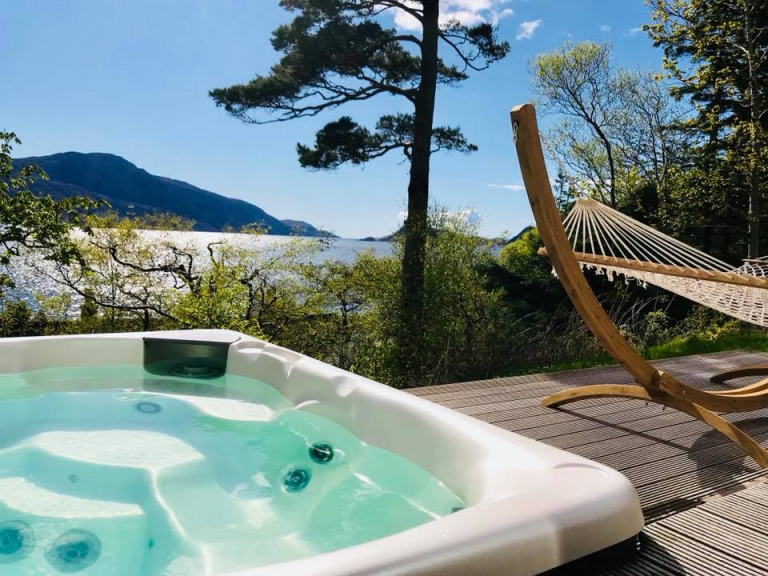 Hot tub and hammock on a deck with lake and mountain view.