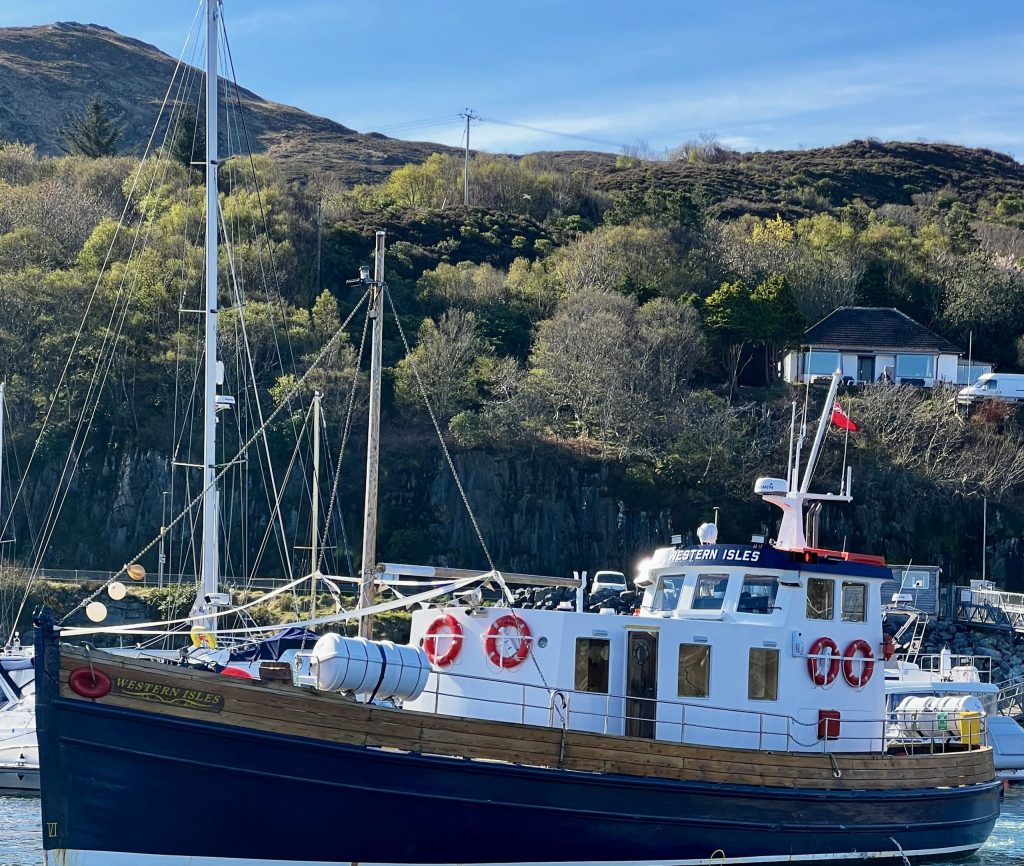 Boat docked in a harbor with hills and trees in the background.