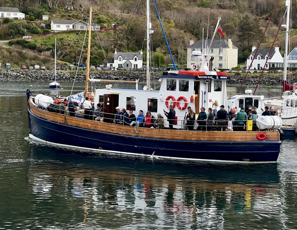 Blue tour boat with passengers, docked near houses on a hillside.