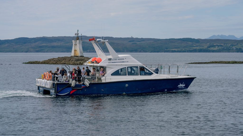 Blue and white passenger boat sailing near a small lighthouse with distant hills.