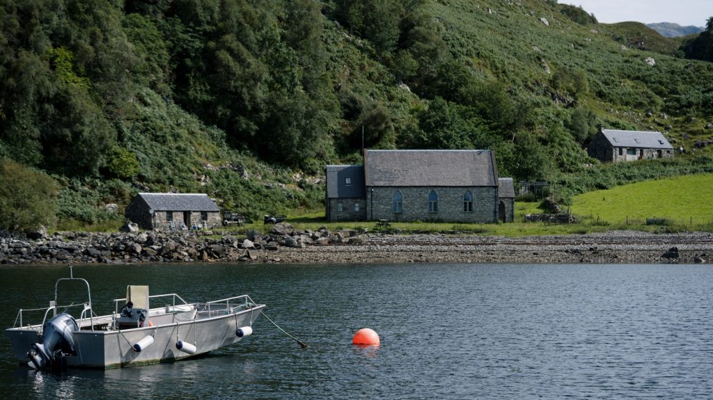 Boat on lake with stone buildings and green hills in background.