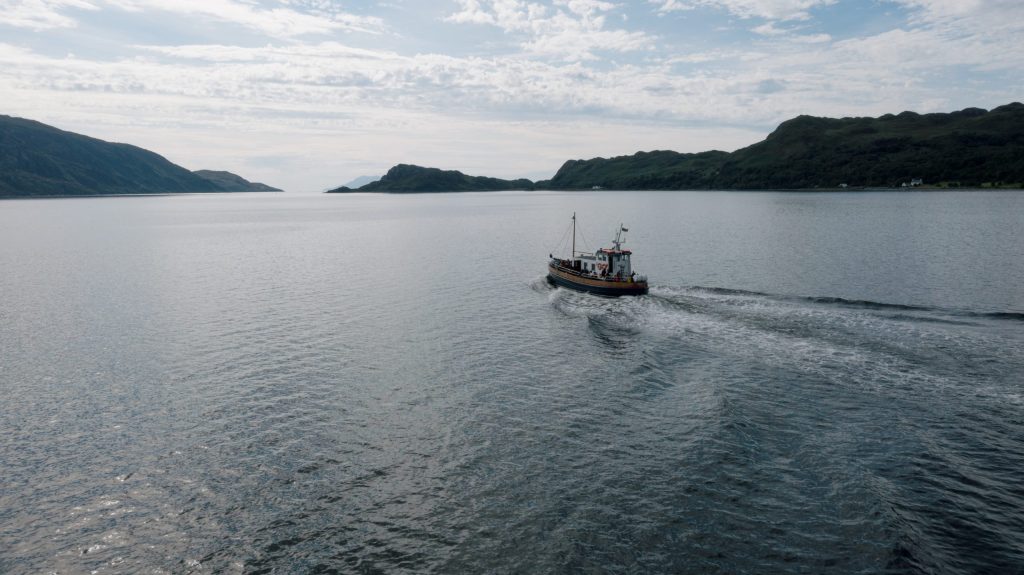 Boat sailing on a calm lake with hilly shoreline in the background.
