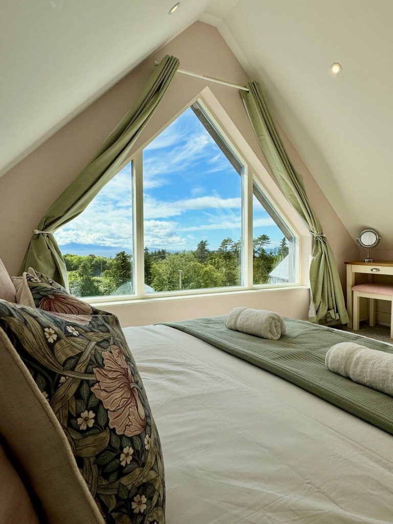 Cozy bedroom with large triangular window and scenic forest view.