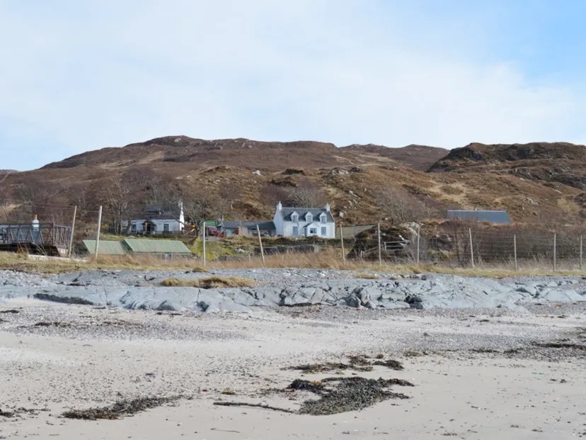 Coastal landscape with houses, hills, and a sandy beach.