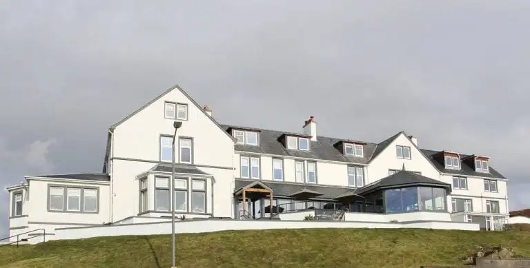 imgi_4_image001-768x389 Large white building on a grassy hill under a cloudy sky.